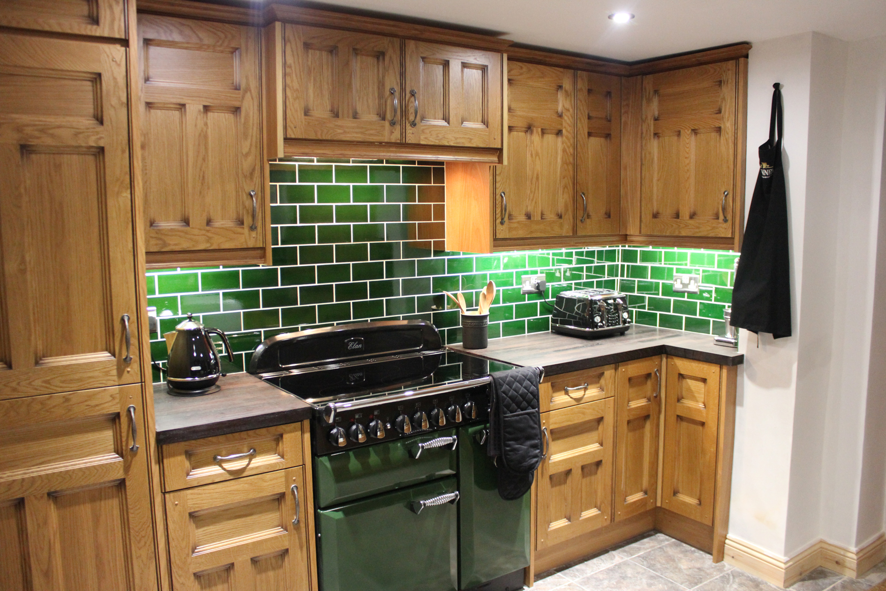 Kitchen with green brick walls and wooden cupboards